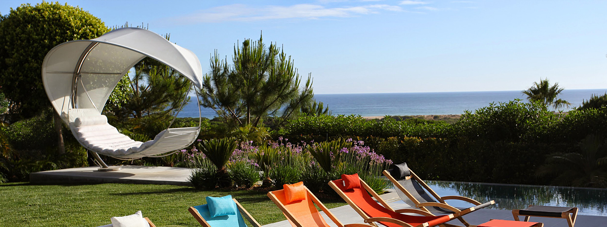 Image of white Wave hammock & Beacher deck chairs by Royal Botania set in lush coastal garden