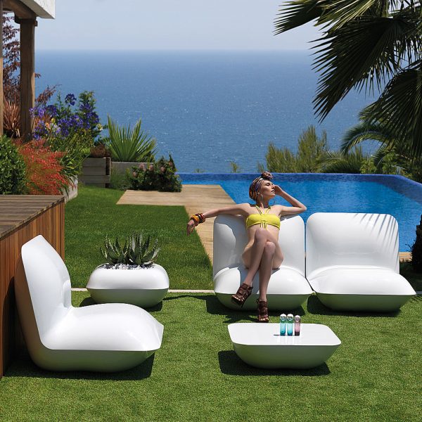 Image of woman lying back on Vondom Pillow modern outdoor lounge furniture in the sun, with palm trees, swimming pool and sea in the background
