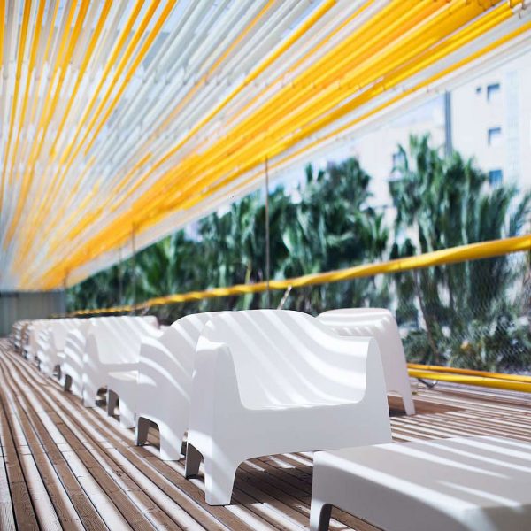 Image of Vondom Solid white stacking outdoor easy chairs and low tables beneath yellow fabric canopy