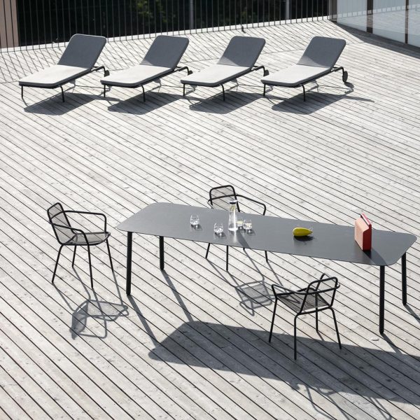 Image of Todus Starling dining table and chairs on decking, with 4 Starling modern sunbeds in the background
