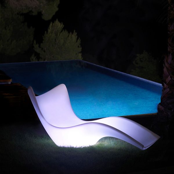 Nighttime image of illuminated white Surf garden chaise by Vondom, with swimming pool in the background