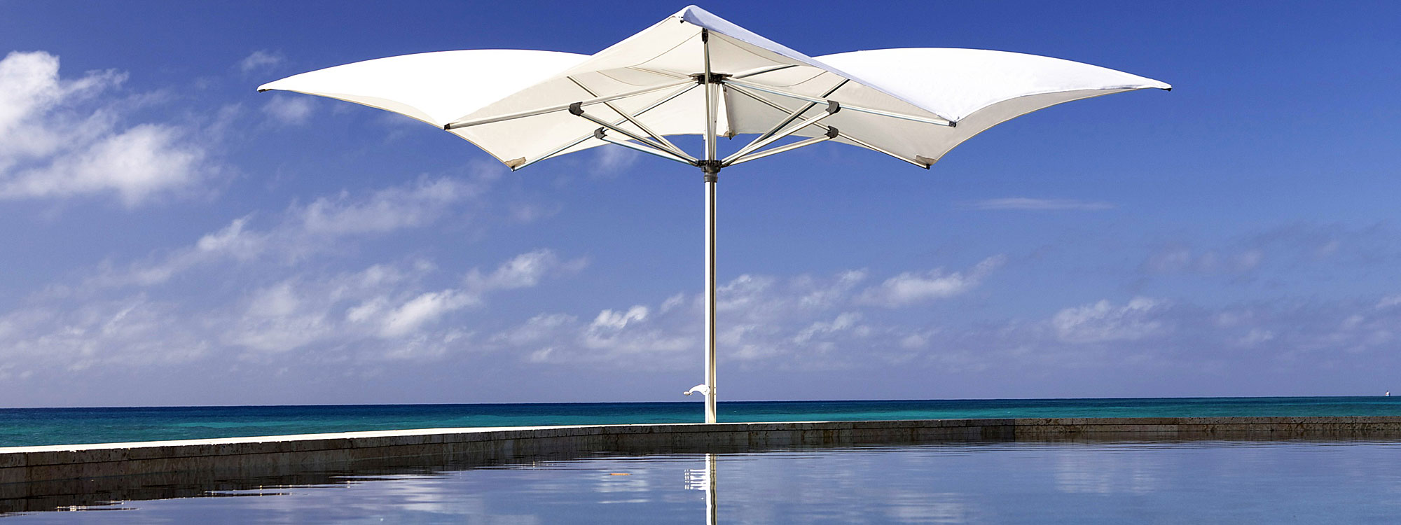 Image of Tuuci Ocean Master Max Manta mast parasol with white canopy and polished titanium mast and ribs, with swimming pool in foreground and sea in background