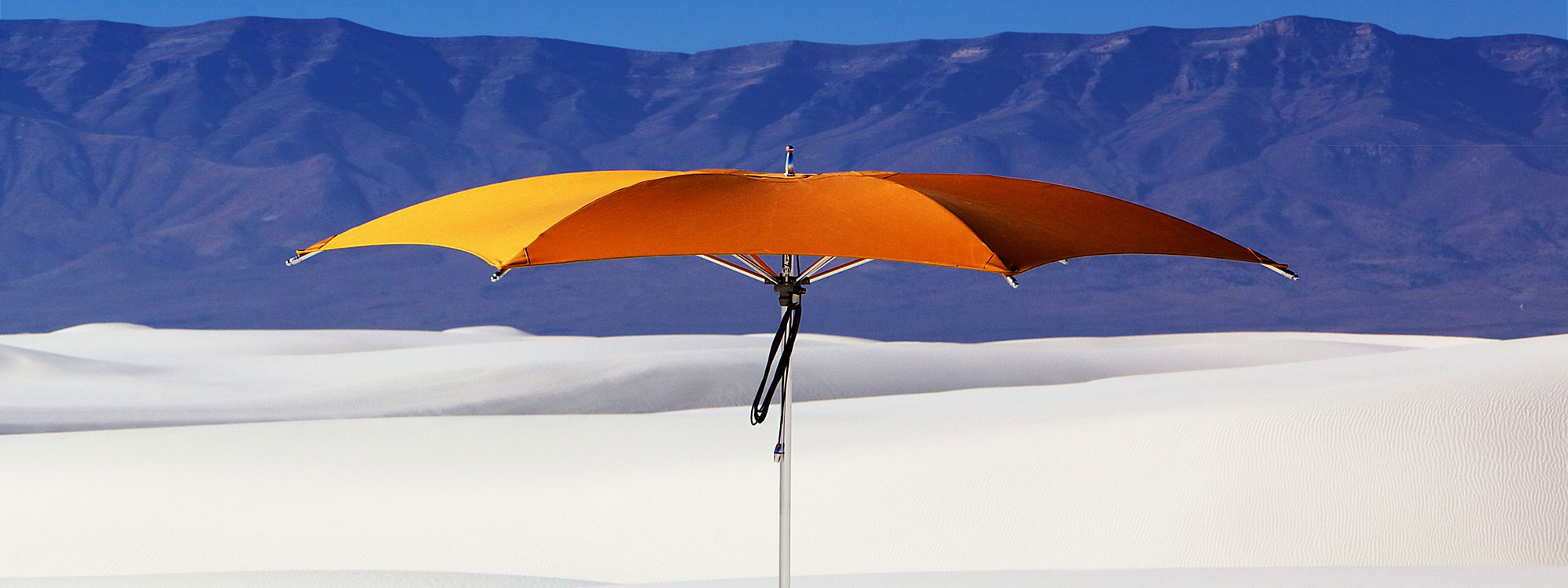 Image of orange Ocean Master Crescent parasol with polished titanium mast and ribs, with sand dunes and mountains in the background