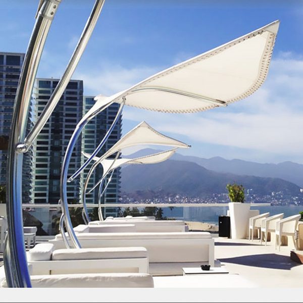 Image of multiple Tuuci Stingray sun canopies installed over white sun loungers, with sea and mountainous coastline in the background