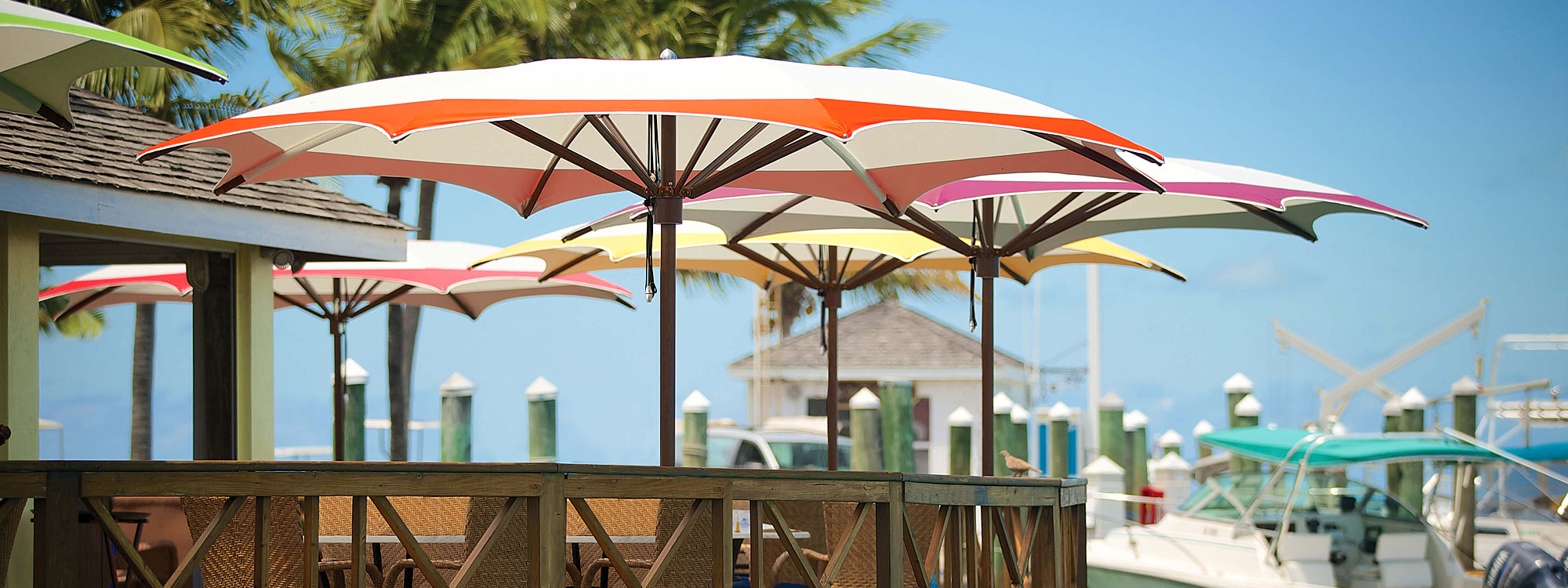Image of octagonal Ocean Master Max center mast parasols with Aluma-Teak mast and ribs and multi-colored canopies, shown on marina restaurant outdoor deck
