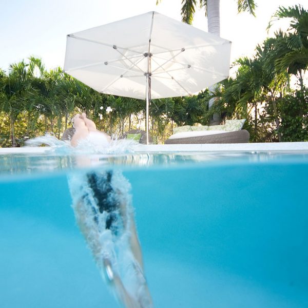 Lady Diving Into Pool In front Of TUUCI Ocean Master Max Centre MAST PARASOLS. MODERN Outdoor Parasol, LUXURY QUALITY Parasols FOR HIGH WINDS & Optional Parasol With HEATER & LIGHTING.