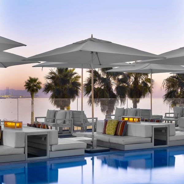 Image at dusk of hotel poolside with square Ocean Master parasols over modern lounge furniture