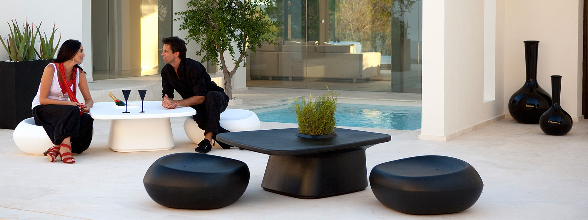 Image of 2 sets of black and white Moma low dining furniture in black and white, shown in tranquil courtyard with swimming pool in the background