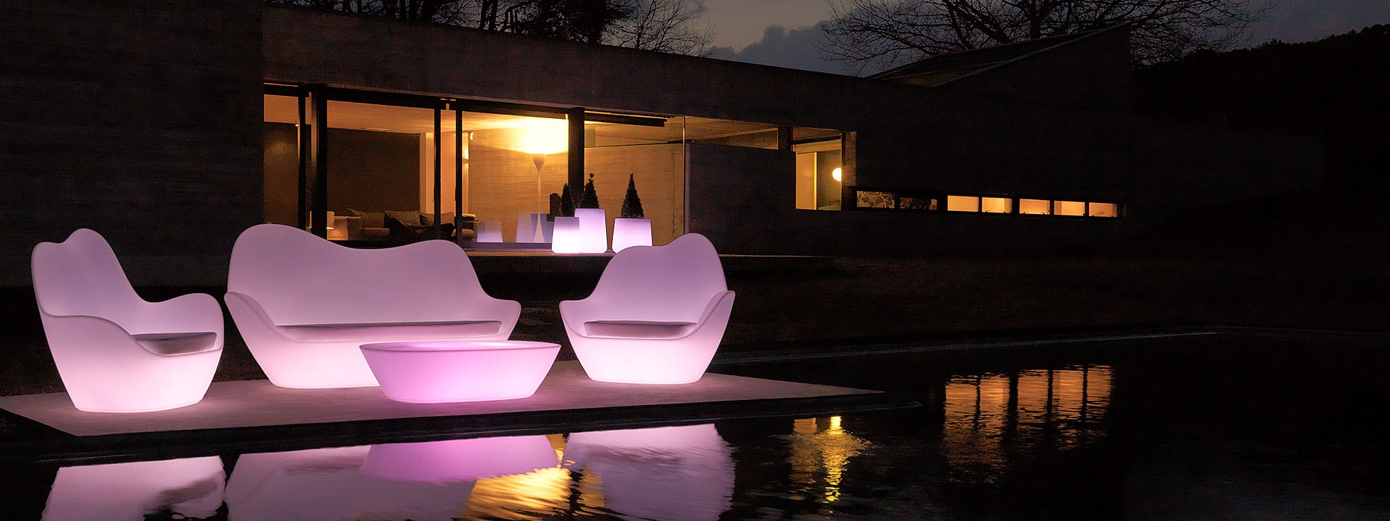 Nighttime image of illuminated Sabinas contemporary roto-molded lounge furniture by Vondom on terrace surrounded by water