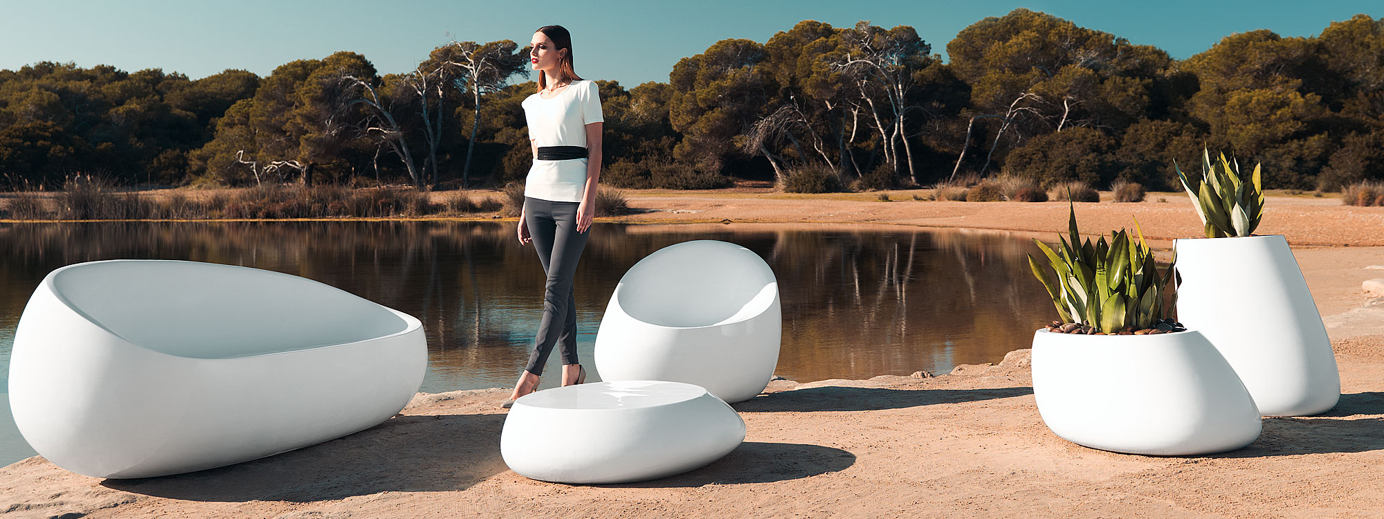 Image of woman stood on arid lakeside next to white Stone garden lounge furniture and modern plant pots by Vondom