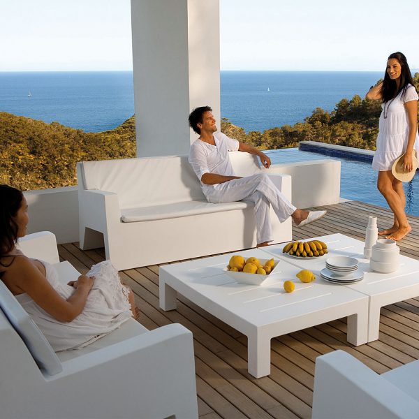 Image of people dressed in white relaxing around white Jut modern plastic garden lounge furniture on terrace at dusk