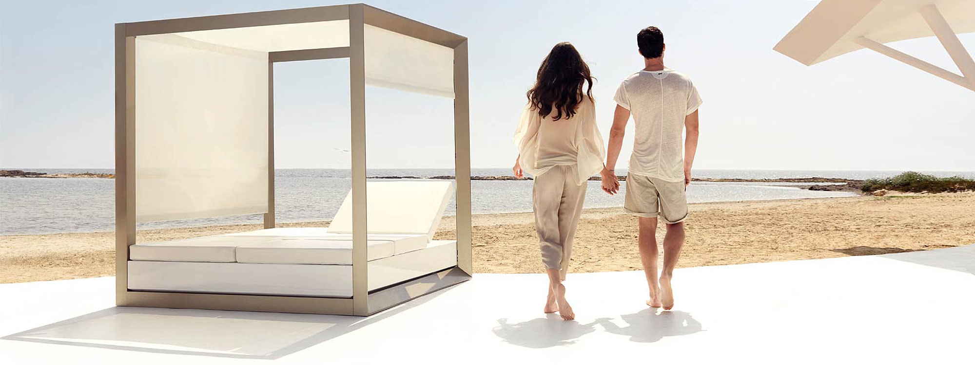 Image of couple on beach walking past Vondom Vela twin daybed with integrated pergola and adjustable blinds