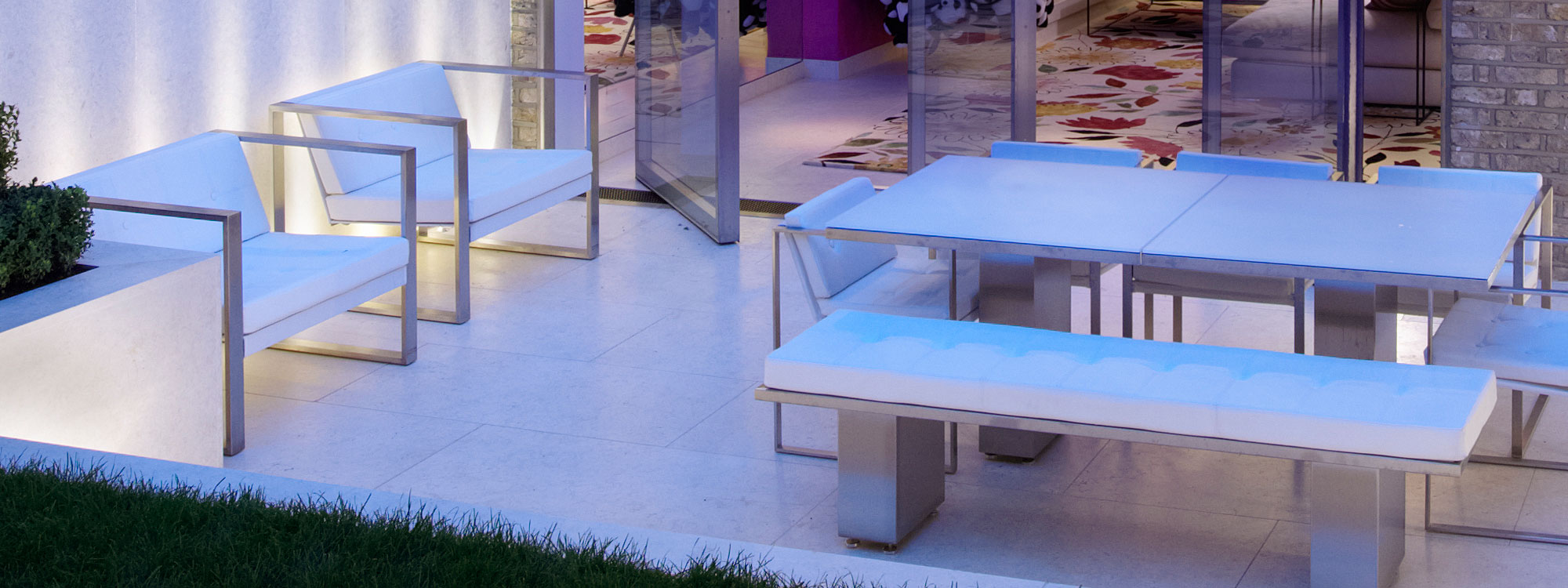 Image of London nighttime terrace, with Poltrona minimalist lounge chairs and Doble pedestal garden table and linear benches by FueraDentro