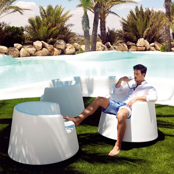 Image of man sat on Roulette white garden rocking chair with swimming pool and palm trees in the background
