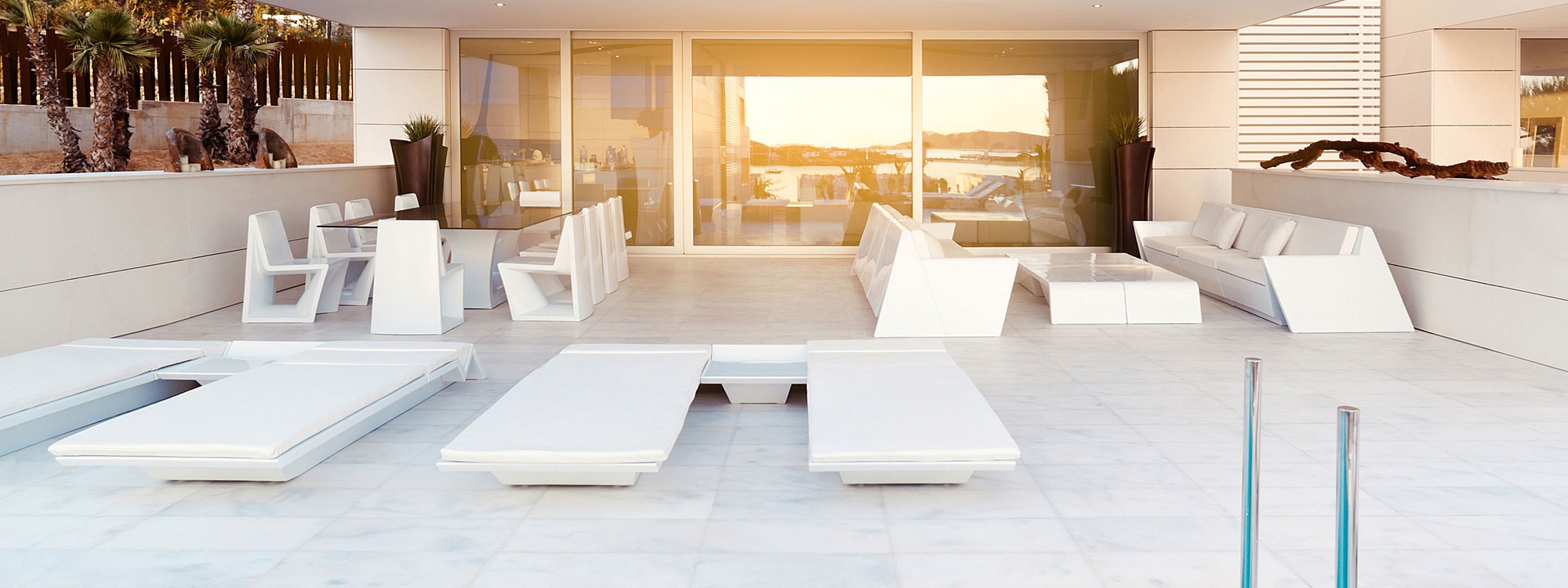Image at dusk of terrace with white Rest sun lpungers and sofas by Vondom