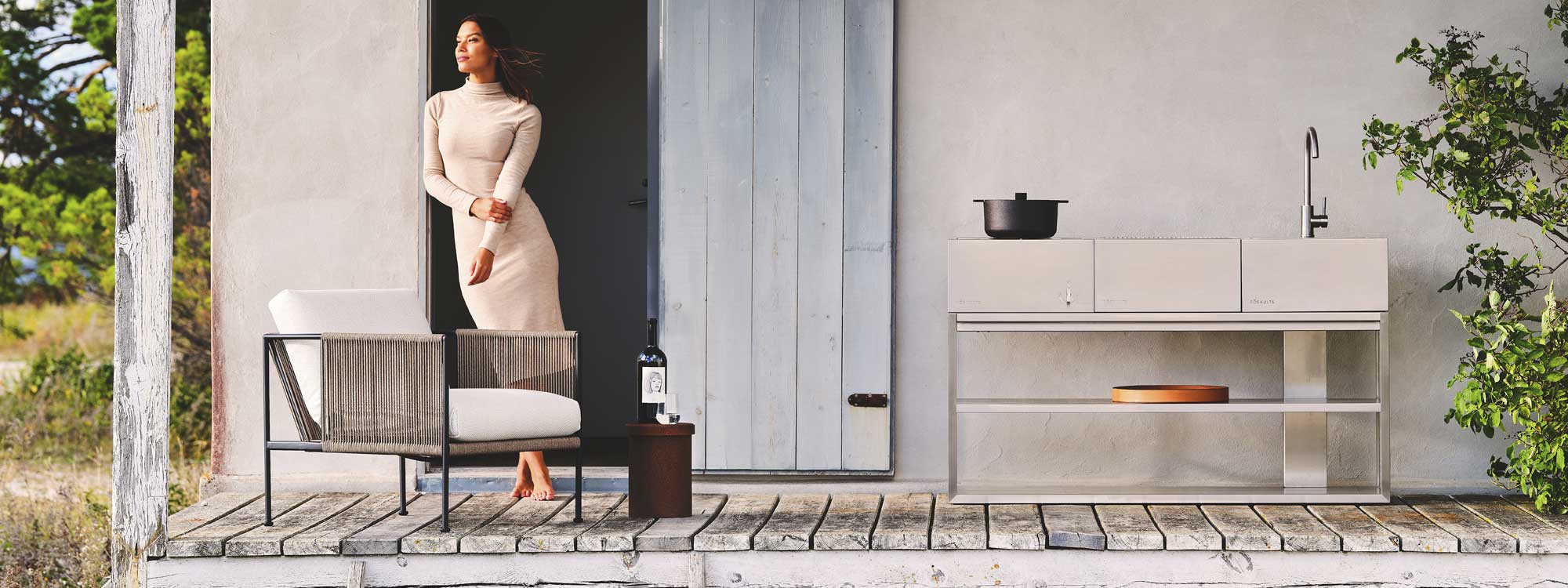 Image of woman leaning against doorway next to Antibes modern garden chair and Open Kitchen stainless steel BBQ