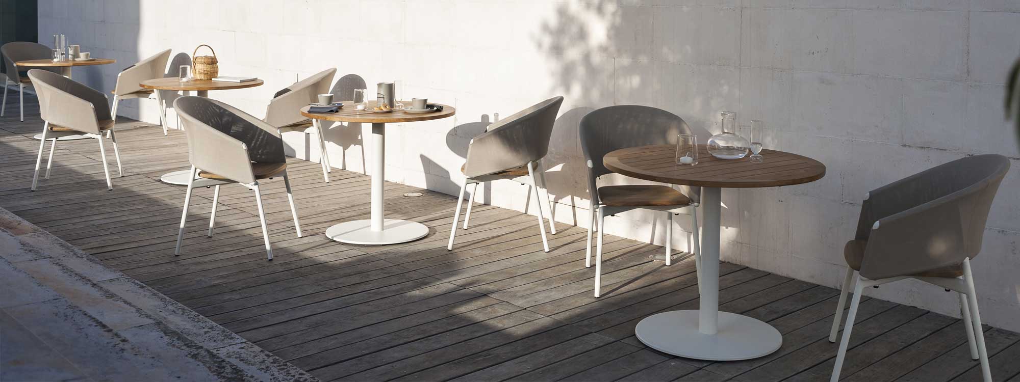 Image of decked outdoor terrace with RODA Stem white bistro tables with teak table tops and Piper Comfort garden chair in white and taupe