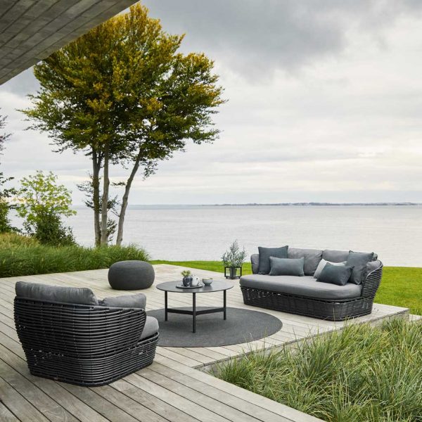 Image of black Caneline Basket cane-effect outdoor lounge furniture, shown on decking with grey sea in background