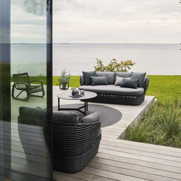 Image of black Cane-line Basket garden sofa and lounge chair on wooden decking, with grey sea and sky in background