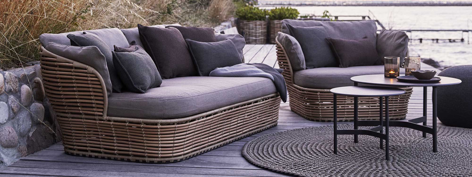 Image of Caneline Basket natural cane-effect garden sofa and lounge chair with taupe cushions, with Twist round low tables in the middle