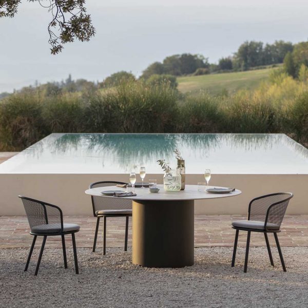 Image of Todus Baza garden chairs an Branta circular outdoor table on terrace, with horizon swimming pool and countryside in background