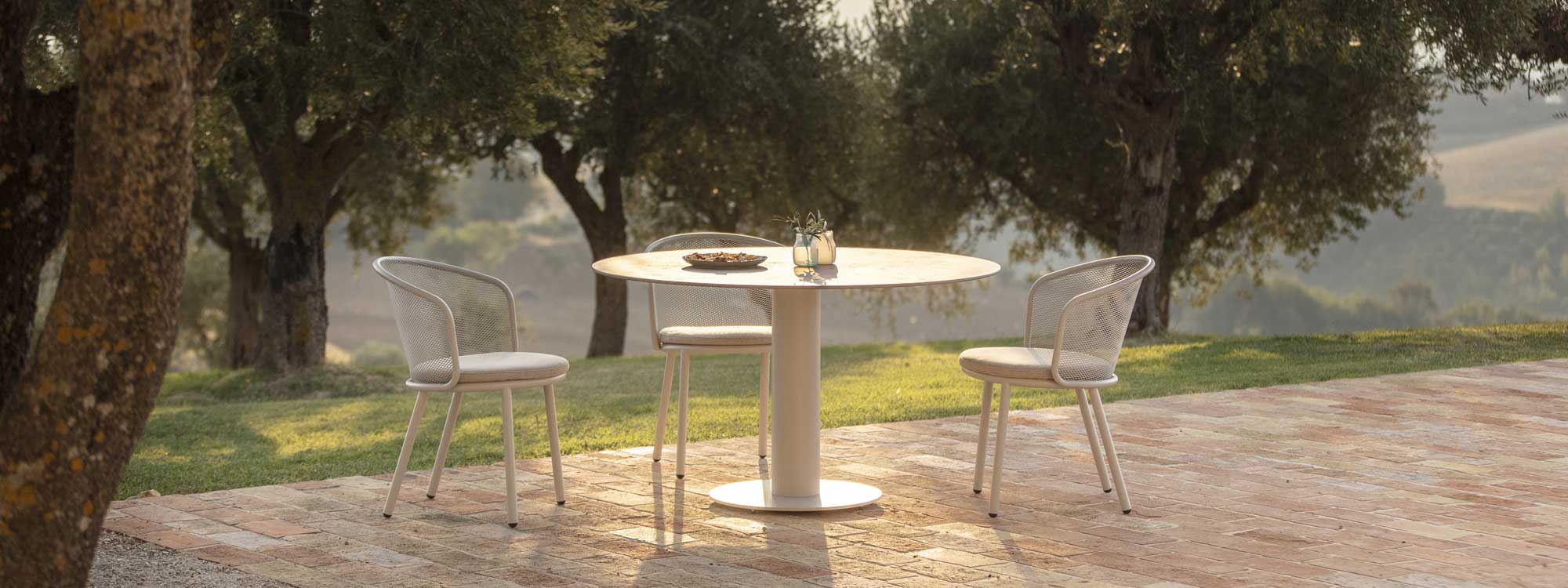Dusk shot of Baza garden dining chair and Branta pedestal table on terrace with olive trees in background
