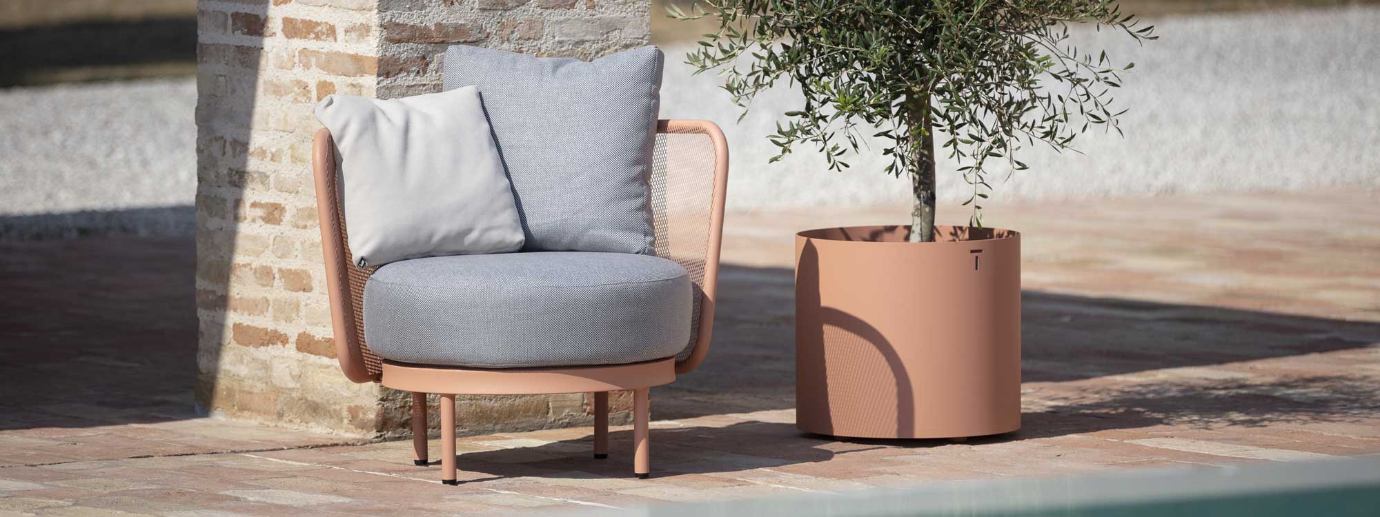 Image of salmon-pink Baza Club modern garden chair and Verdi contemporary planter with small olive tree within