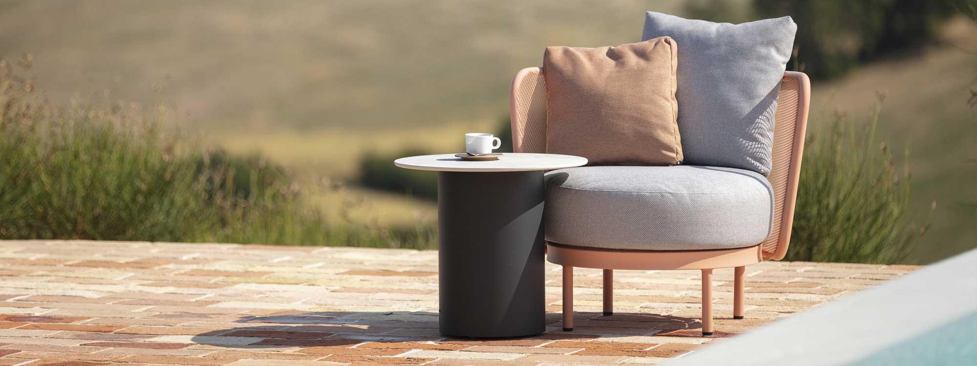 Image of salmon-pink Baza Club garden lounge chair with light-grey and pink cushions, shown together with Branta modern side table with anthracite base