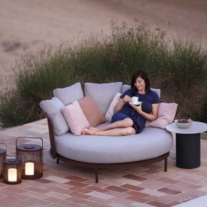 Image of woman drinking a coffee whilst lying on Baza outdoor daybed on terrace, in fading daylight