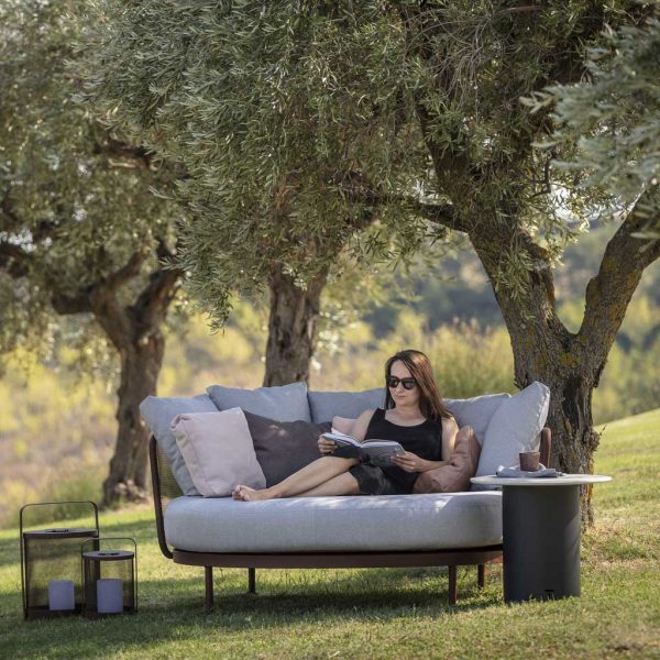 Image of woman lying on Todus Baza outdoor daybed in shade of olive tree
