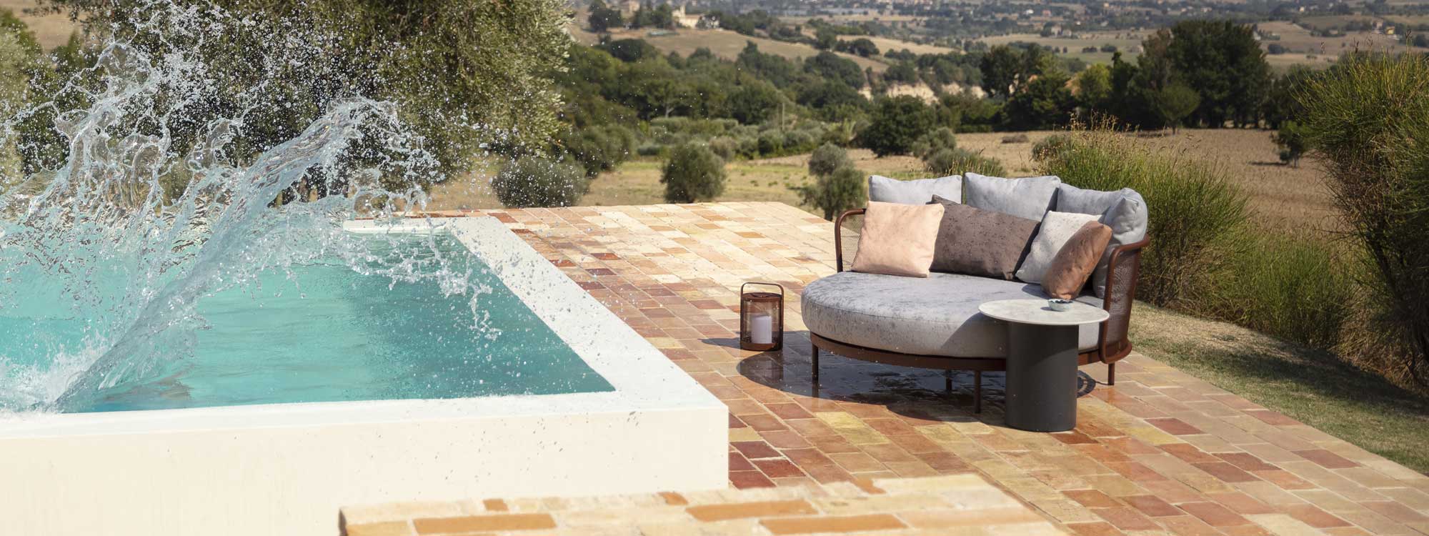 Splashes from swimming pool wet the Baza minimalist garden daybed, with Portuguese countryside in background
