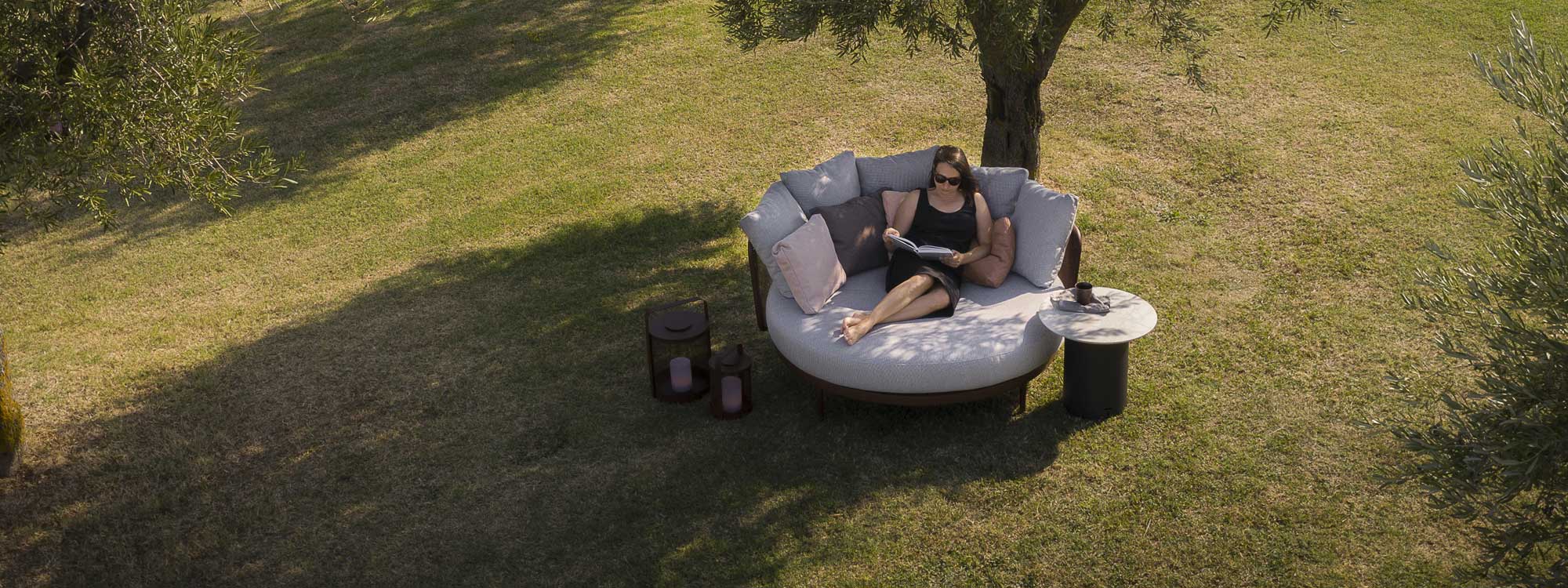 Woman relaxing on Baza luxury garden daybed beneath shade of tree