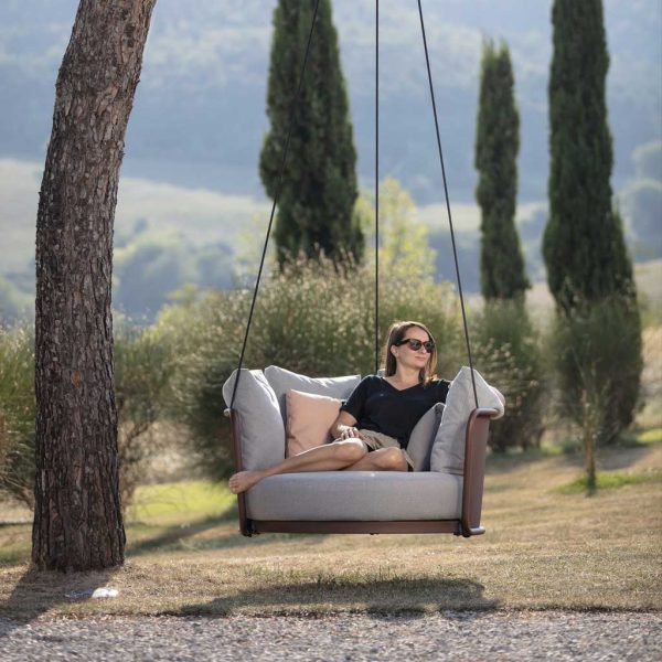 Woman relaxing in Baza garden swing seat on hot summer's day with Cyprus firs in background