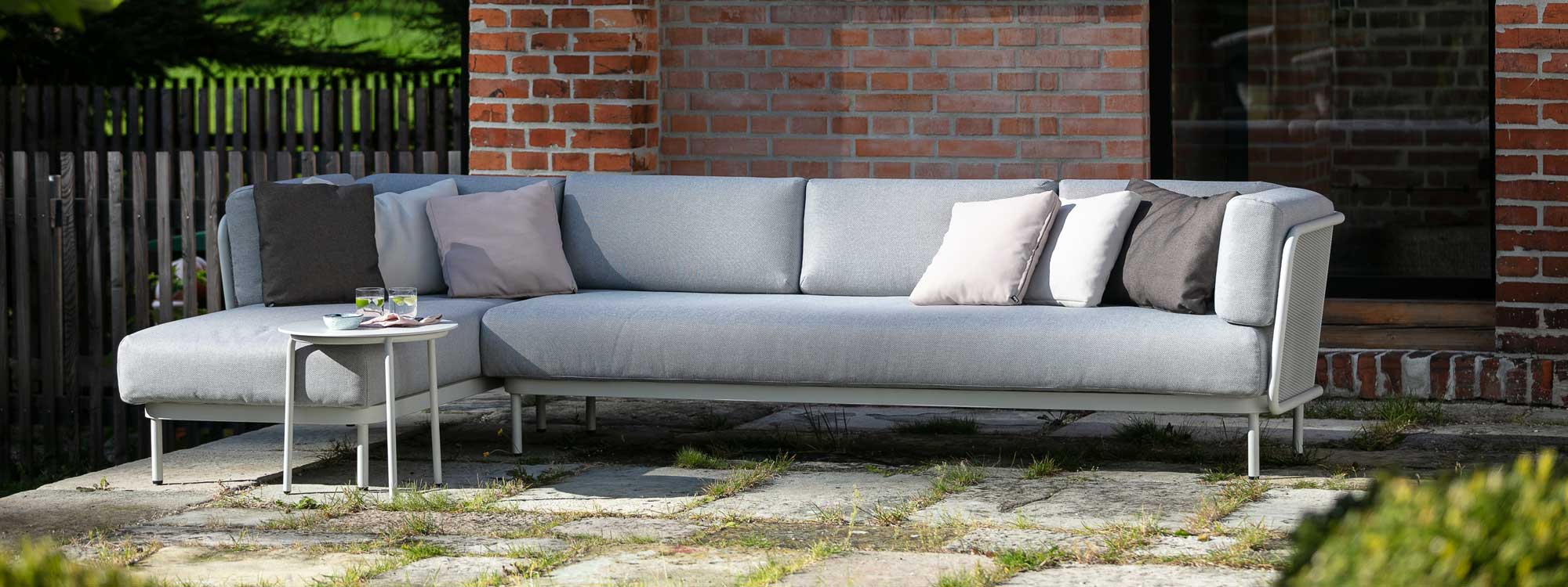 Image of Baza white garden sofa with grey cushions in flag stoned courtyard