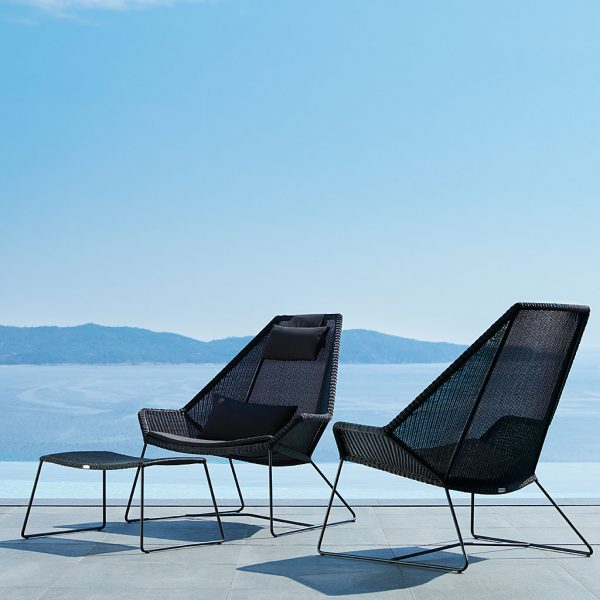 Image of pair of black Cane-line Breeze high-backed garden relax chairs and foot stool on terrace, with hazy Mediterranean sea in background