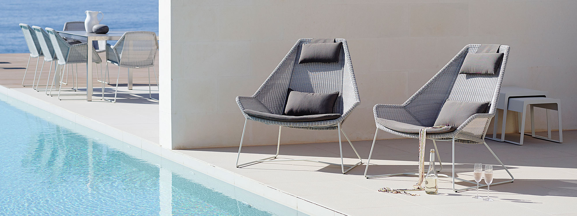 Image of pair of White-Grey high backed Breeze exterior lounge chairs on poolside, with Breeze garden dining chairs by Cane-line in background