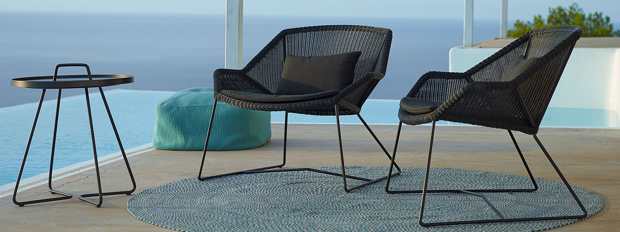 Image of pair of Cane-line Breeze black woven garden lounge chairs with turquoise Divine garden pouf and black On The Move side table