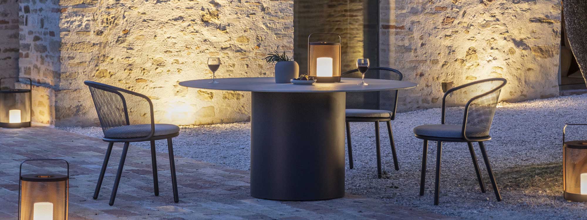 Image of balmy courtyard in light of dusk with Branta round garden table and Baza garden chairs in dark grey
