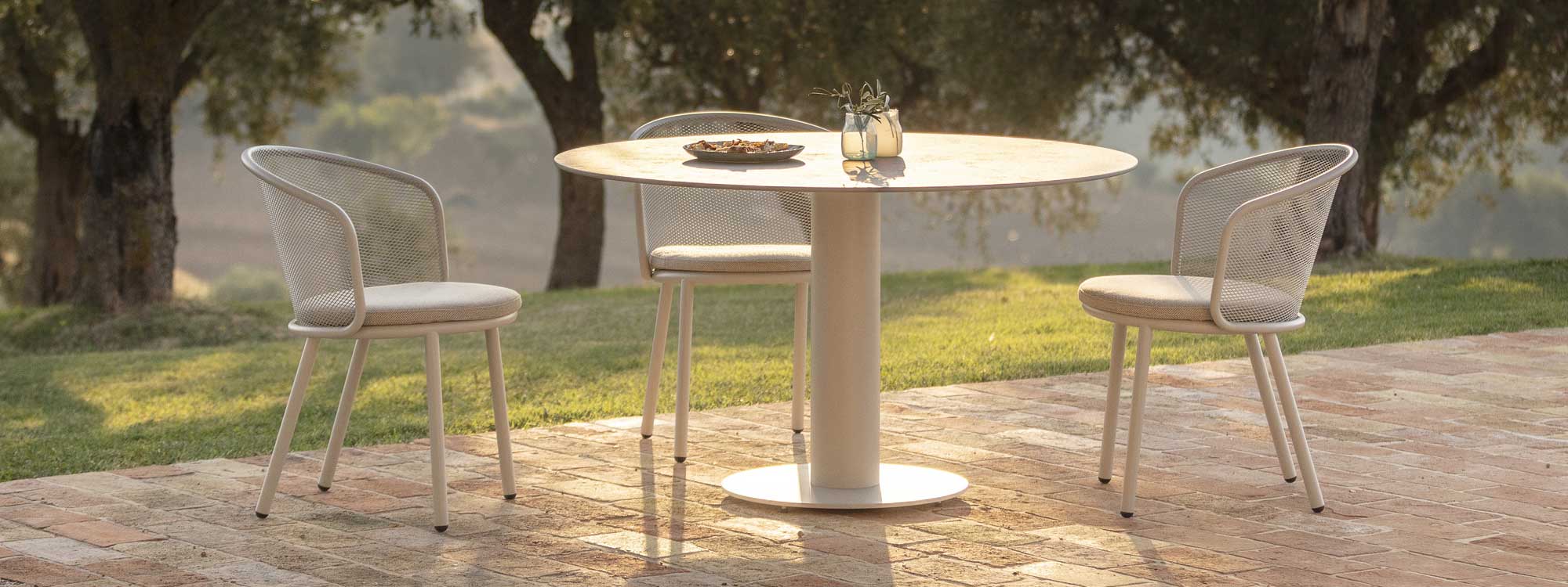 White Branta circular outdoor table and Baza garden chair in warm evening sunlight