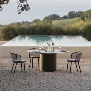 Image of Baza modern garden Chairs & Branta CIRCULAR GARDEN TABLE on gravel, with swimming pool and countryside in background on summer's evening