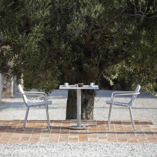 Image of Branta small white garden table and Starling white garden armchairs on sunny terrace with large tree in background