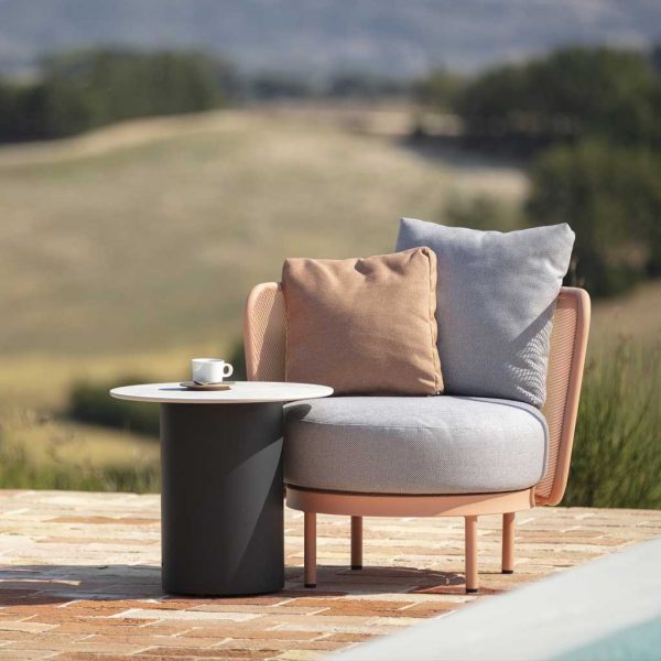 Image of salmon pink Baza outdoor lounge chair and Branta round side table on sunny poolside with arid hills and countryside in the background