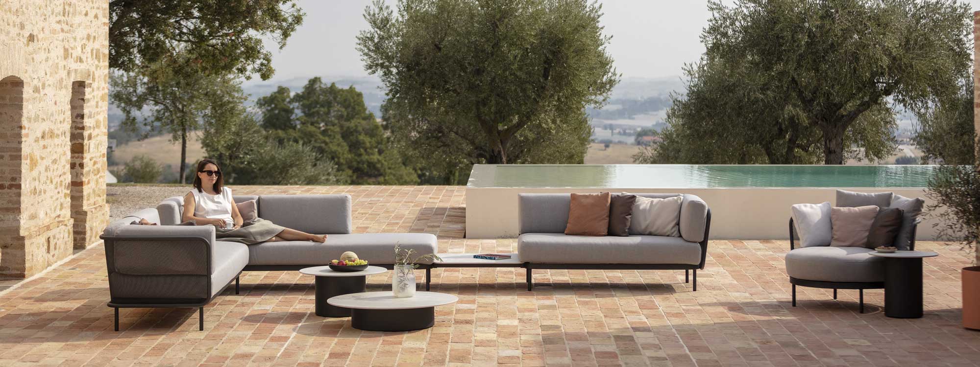 Baza modern garden sofa set with Branta low tables on sunny terrace with swimming pool and olive trees in background