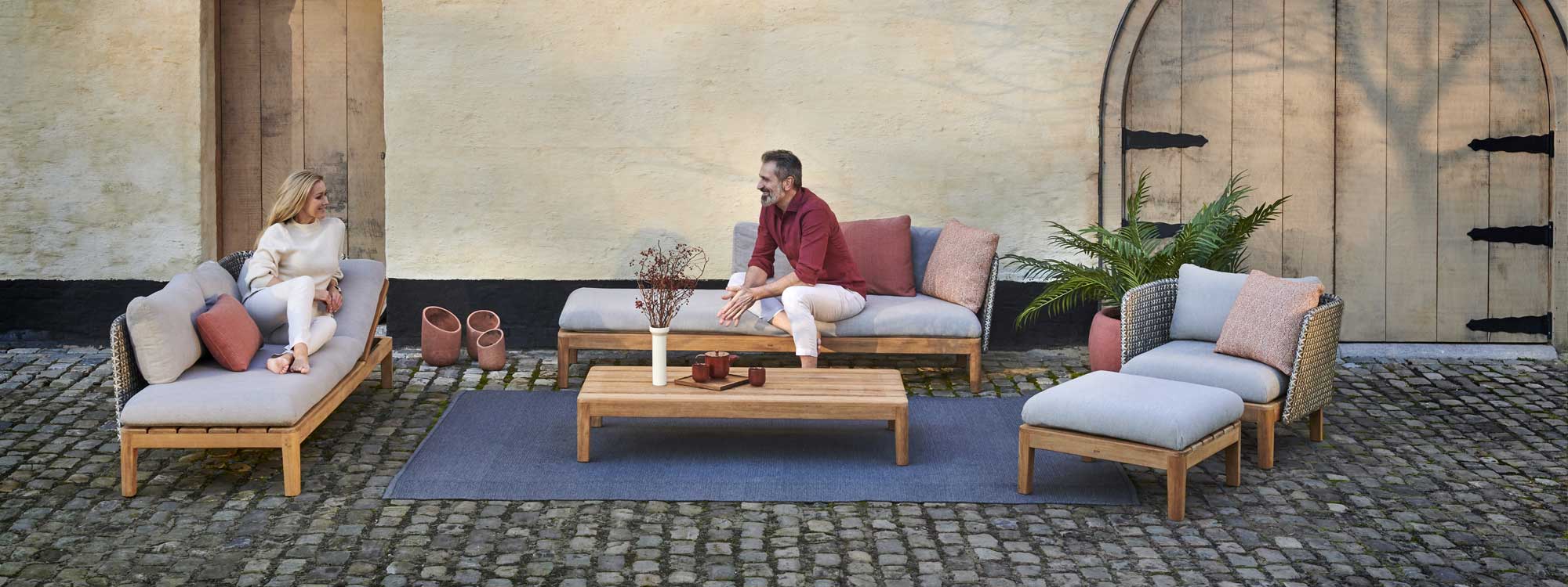 Image of couple chatting on Calpyso garden lounge furniture by Royal Botania in cobbled courtyard