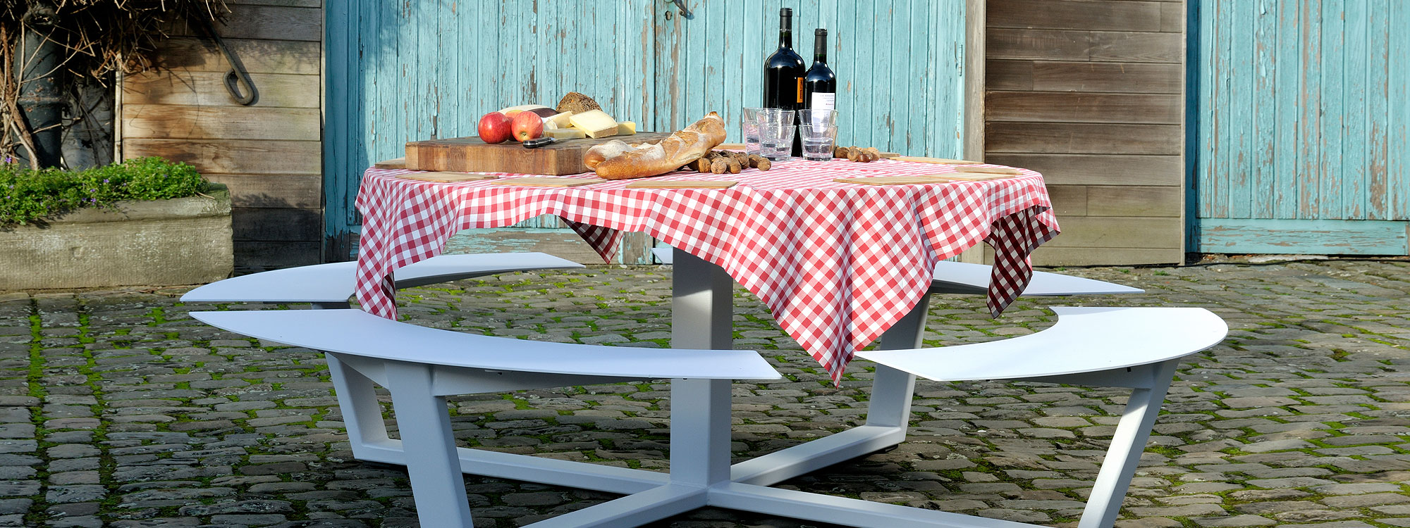 Image of Cassecroute's La Grande Ronde round picnic table in white, with table top set with red & white gingham table cloth and wine and cheese