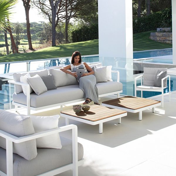 Image of woman sat reading on white Alura garden sofa with Alura teak low tables in front of her by Royal Botania