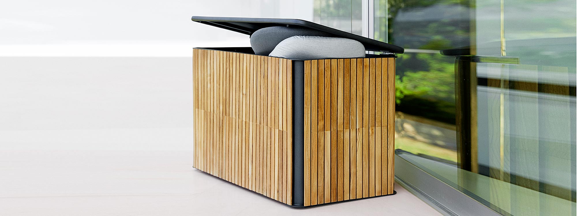 Image of Cane-line cushion box in Lava-grey aluminum with teak slats, shown with lid ajar and cushions poking out
