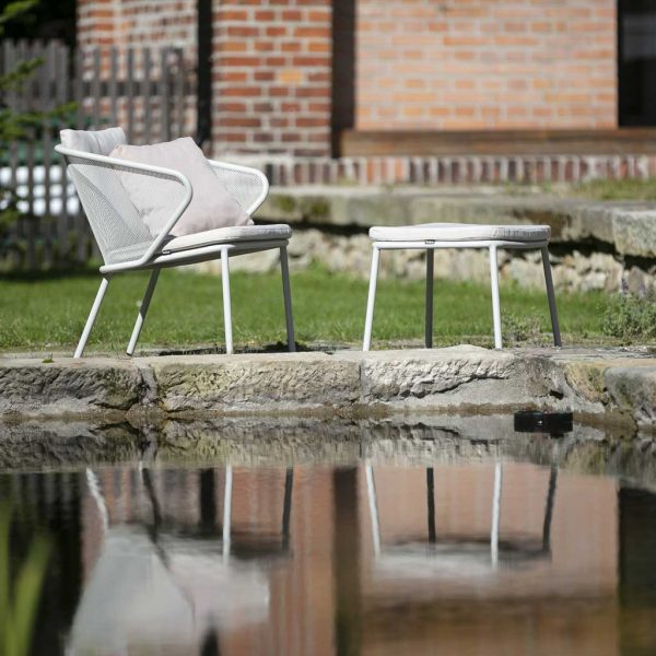 Image of Todus Condor modern garden chair and foot stool with reflection shown in water feature