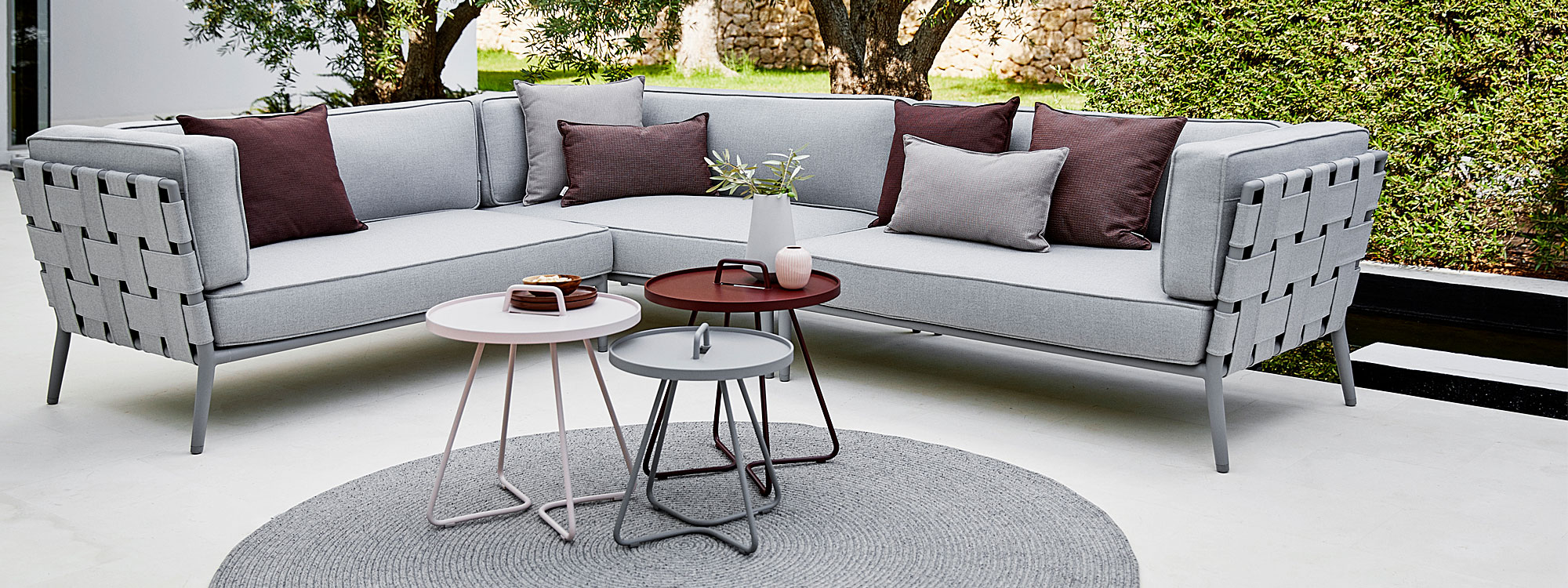 Image of grey and burgundy On The Move tray tables and grey Core garden sofa by Cane-line