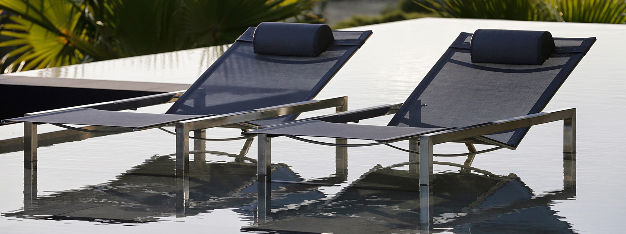 Image of pair of Ninix sun loungers with electro-polished stainless steel frames and black seats and backs sat in water of swimming pool by Royal Botania